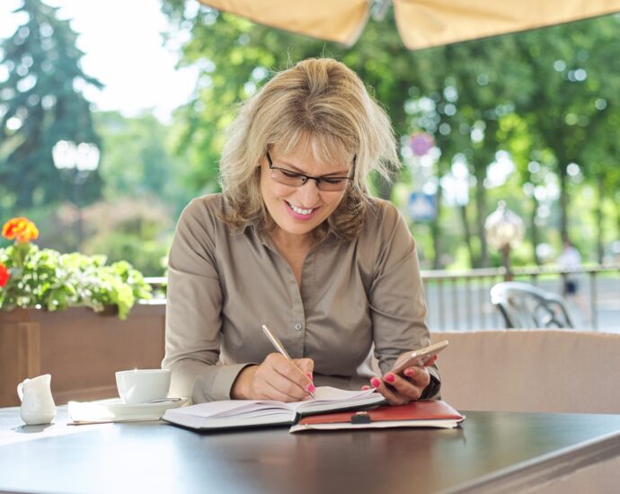Business beautiful woman writing in business notebook using smartphone