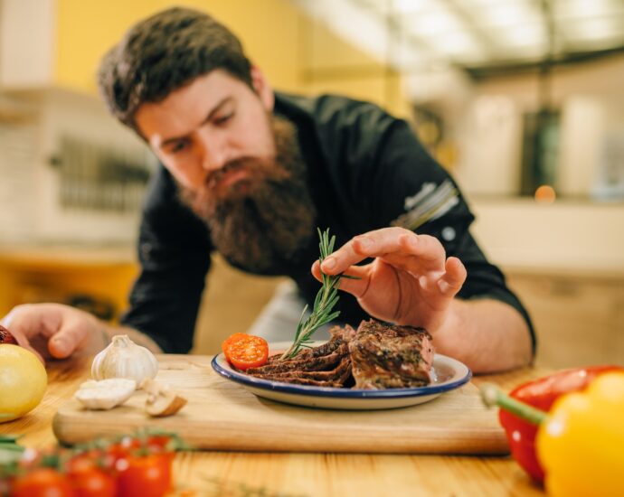 Chef decorates herbs roasted meat slices in plate