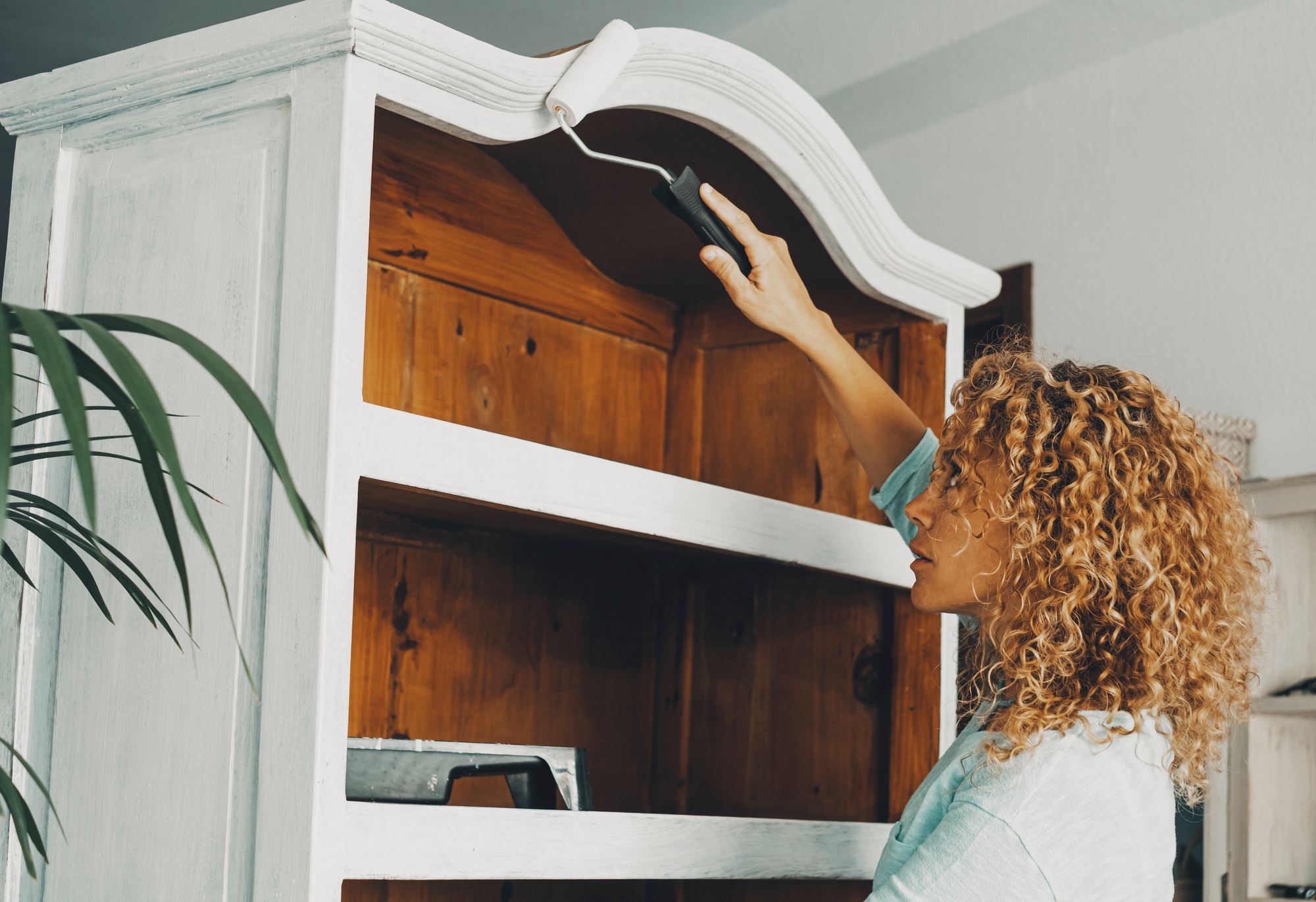 One adult woman in indoor leisure hobby activity painting an old wooden cabinet furniture alone
