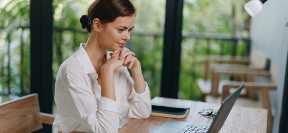 Smiling Freelancer Working on Laptop at Home Office A cheerful young woman with a laptop sits at her