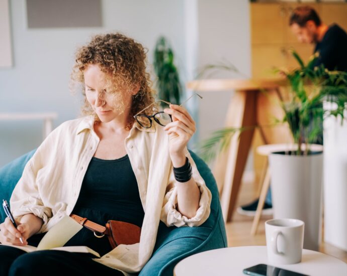 Woman puts on glasses and writes in paper notebook