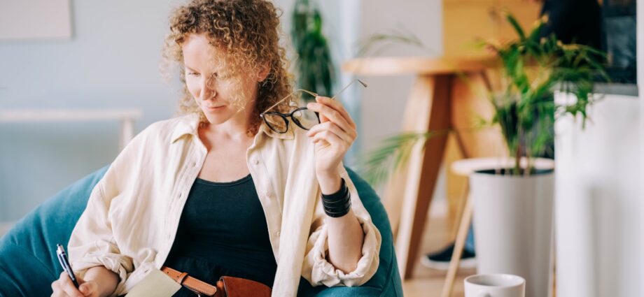 Woman puts on glasses and writes in paper notebook